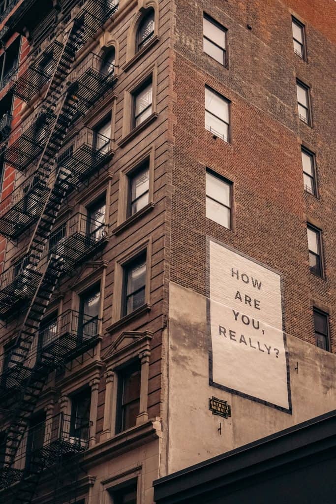 Image of the side of a apartment building like in new york with a sign that reads, "how are you really?" S4 E20 - Struggle Engaging? You Might Be Languishing Or Dormant